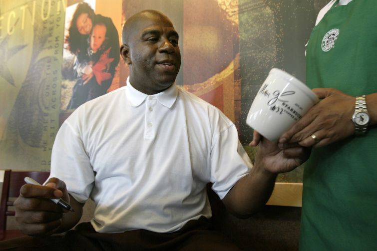 A man sitting down, taking a coffee mug from someone, and preparing to sign it.