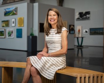 A woman sitting on a bench in a gallery, smiling.