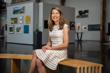 A woman sitting on a bench in a gallery, smiling.