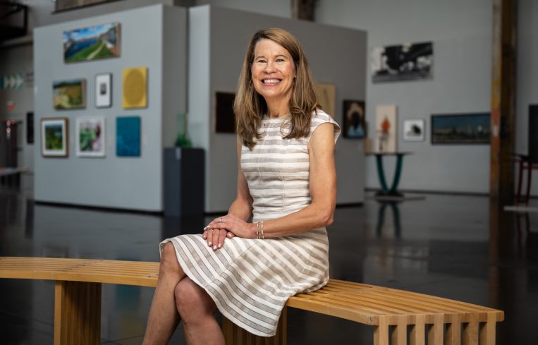 A woman sitting on a bench in a gallery, smiling.