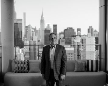 A man standing in a living room with buildings behind him.