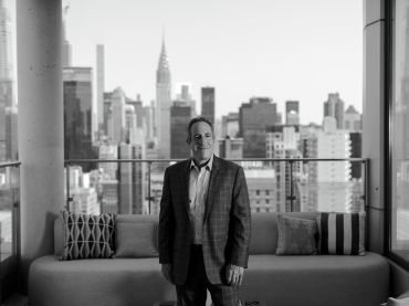 A man standing in a living room with buildings behind him.