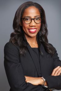 A woman smiling with glasses and her arms folded. 