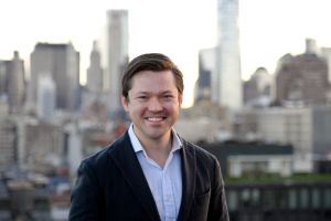 A man smiling with buildings behind him. 