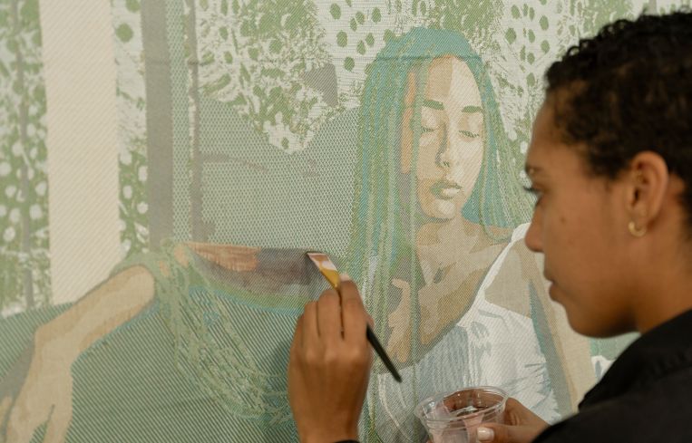 Malaika Temba holds a paintbrush to one of her unfinished textile pieces.