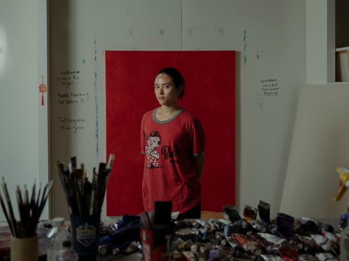 Gwen Hollingsworth stands in front of one of her oil paintings in a red T-shirt.