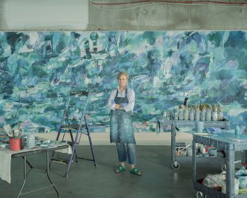 Kerry Irvine stands in front of an oversized canvas wearing a blue apron.
