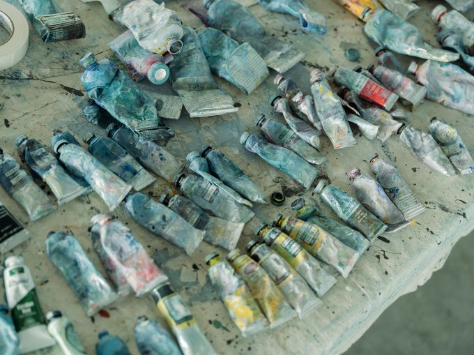 Several rows of half empty tubes of oil paint lie on a table.