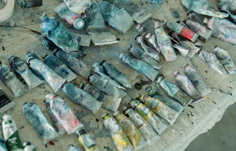 Several rows of half empty tubes of oil paint lie on a table.