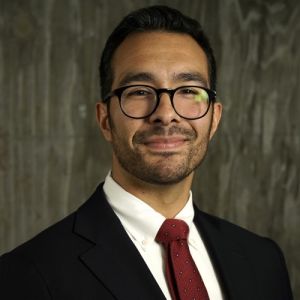 A man in glasses and a suit, smiling.