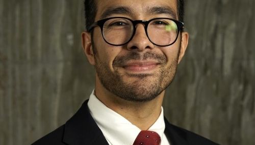 A man in glasses and a suit, smiling.