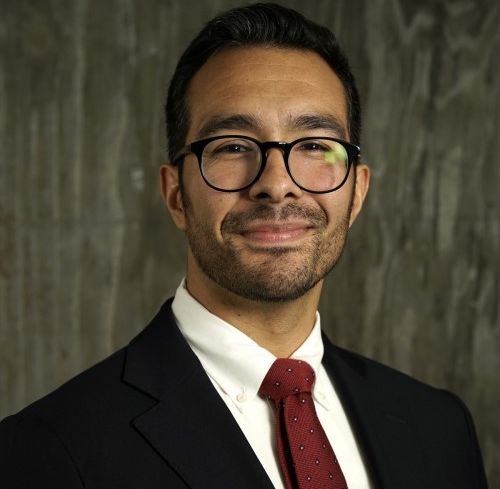 A man in glasses and a suit, smiling.