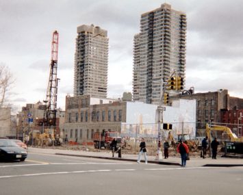 A construction site from a distance, with two towers rising behind it and a fence around it.