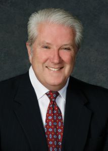 A man in a suit with white hair smiling.