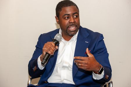 A man sitting down with a microphone in one hand, talking.