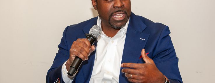 A man sitting down with a microphone in one hand, talking.