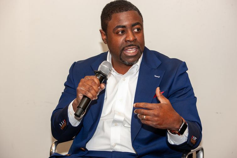 A man sitting down with a microphone in one hand, talking.