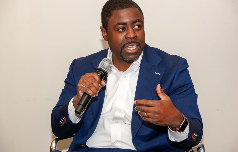 A man sitting down with a microphone in one hand, talking.