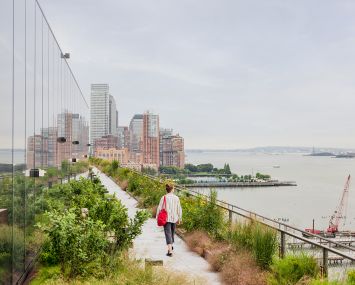 A person strolling along a terrace that's next to a wide river.