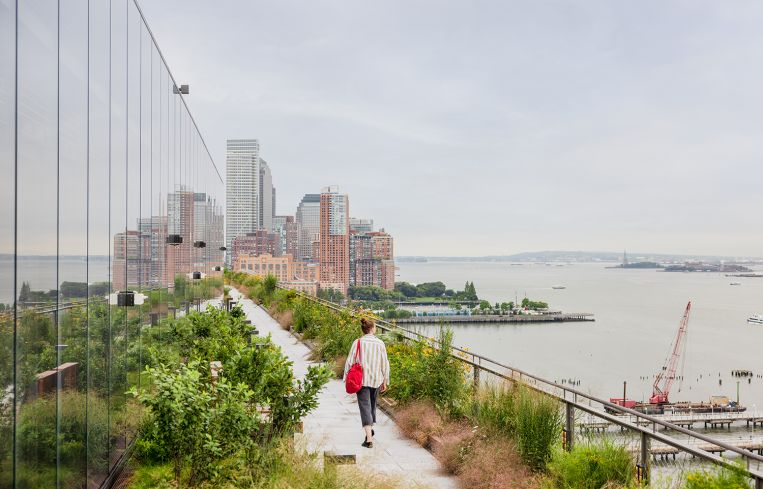 A person strolling along a terrace that's next to a wide river.