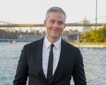 A man in a suit with a bridge in the distance behind him.