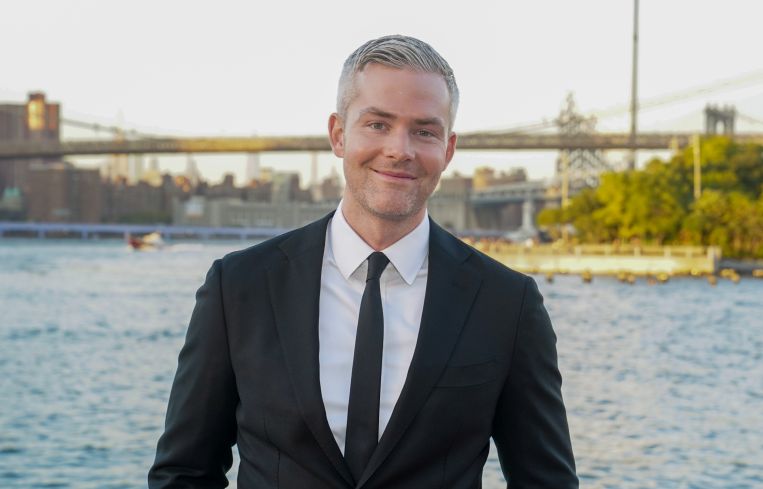 A man in a suit with a bridge in the distance behind him.