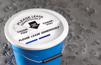 Charity collection bucket that read "Please Lease Generously."