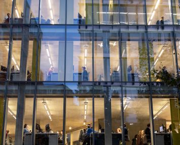 People working at their desks in an exterior night view of an office building.