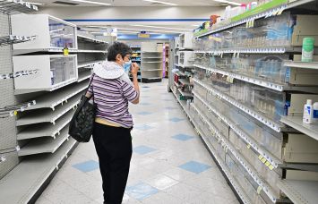 A woman browses through what items remain on near empty shelves at a pharmacy.