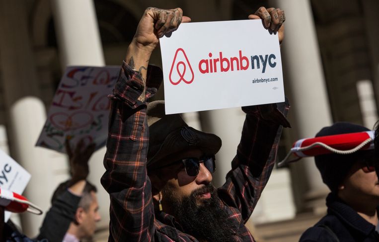 A man holds an Airbnb NYC sign at a rally.