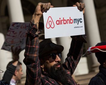 A man holds an Airbnb NYC sign at a rally.