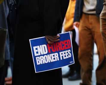A hand holding a sign that says End Forced Broker Fees.