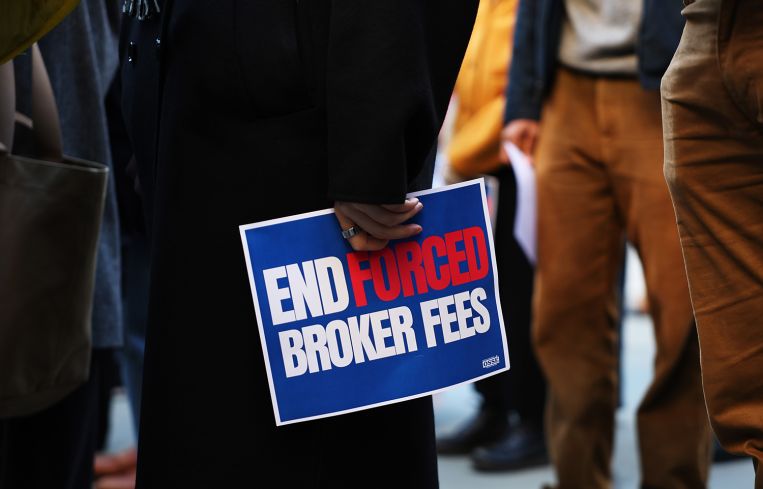 A hand holding a sign that says End Forced Broker Fees.