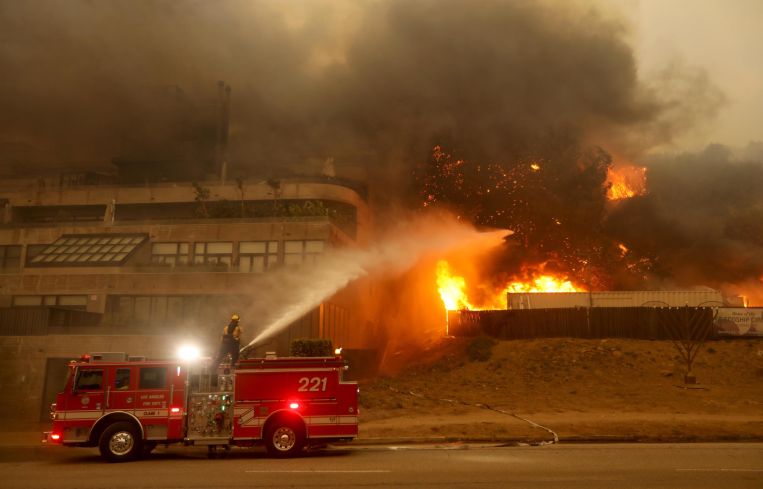 A firefighter tries to put out a portion of the Pacific Palisades fire that threatens a nearby building along Sunset Boulevard In Pacific Palisades.