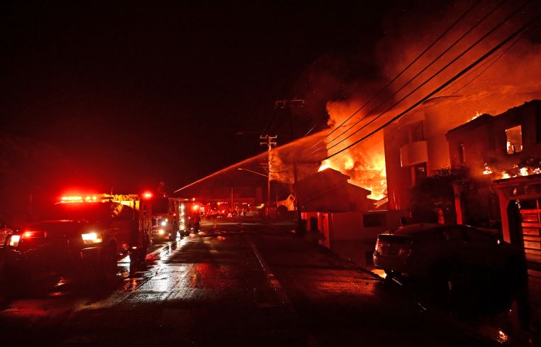 Firefighters work to put out a blaze as homes burn along Pacific Coast Highway during the Palisades Fire in Malibu, California.