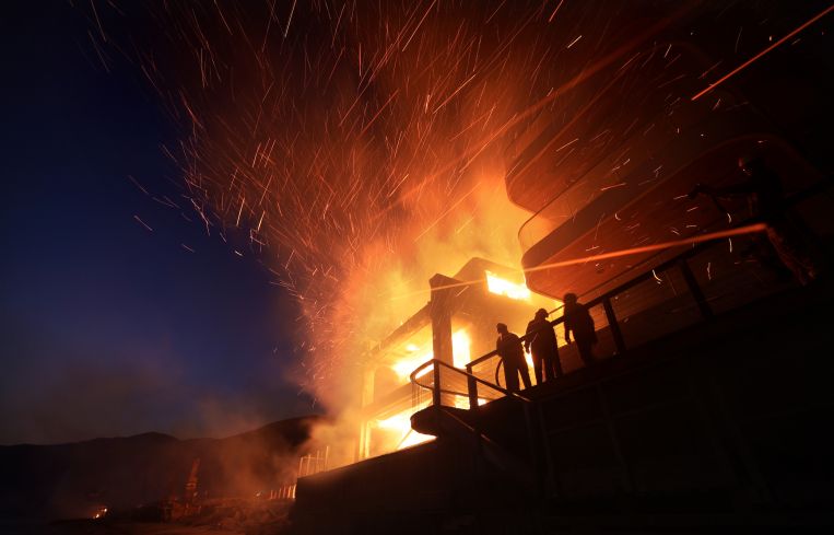 A firefighter battles a house fire along PCH as the Palisades Fire burns in Malibu.