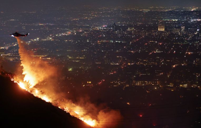 A firefighting helicopter drops water as the Sunset Fire burns in the Hollywood Hills with evacuations ordered on January 8.