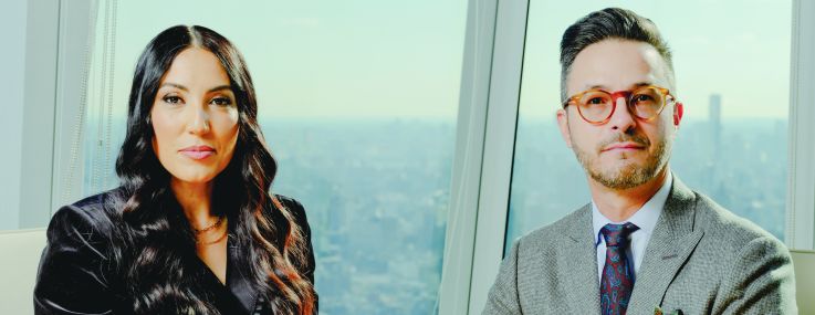 A woman and a man next to each other at a conference table with a city skyline in the background.