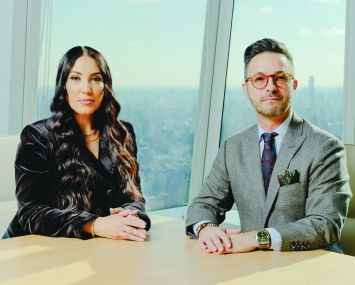 A woman and a man next to each other at a conference table with a city skyline in the background.