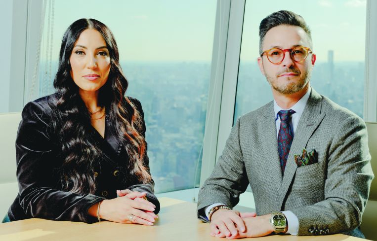 A woman and a man next to each other at a conference table with a city skyline in the background.