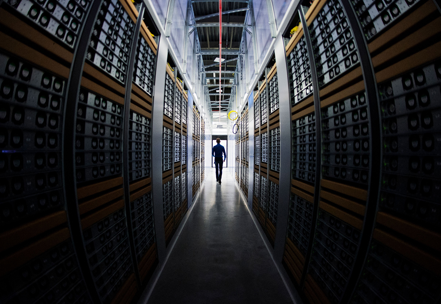 A man walking down a row of servers in a data center.