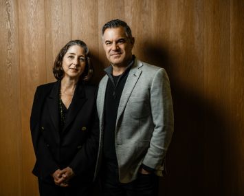 A woman and a man standing side by side in front of a wooden wall.