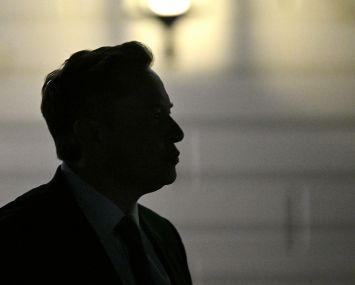 Elon Musk is silhouetted as he departs the White House.