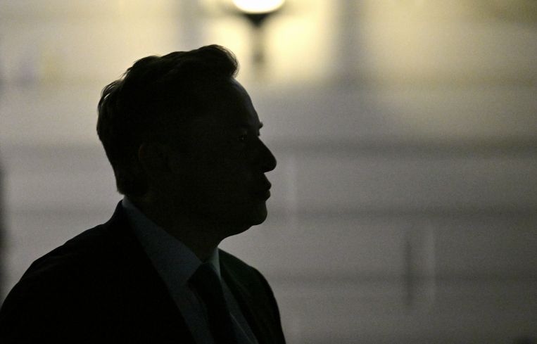 Elon Musk is silhouetted as he departs the White House.