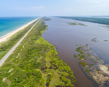 A long highway in between an ocean and lush vegetation, as seen from the air.