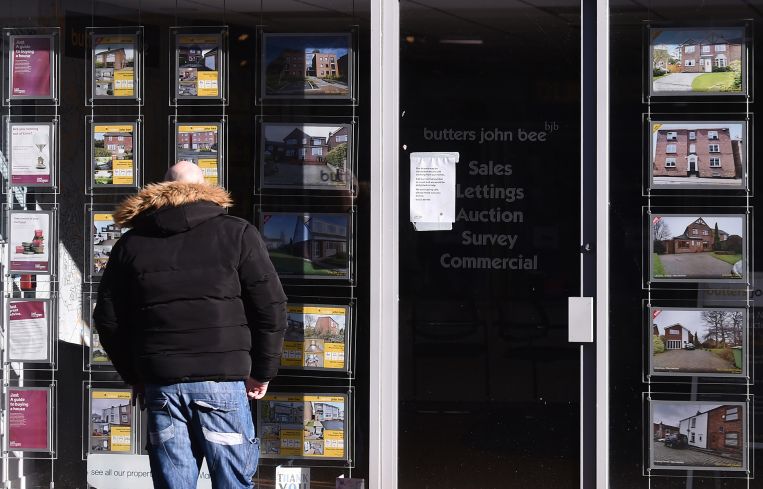 A man looks at advertisements for houses displayed in a window.