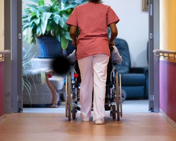 A resident of a nursing home is pushed along a corridor by a nurse.