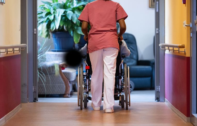 A resident of a nursing home is pushed along a corridor by a nurse.