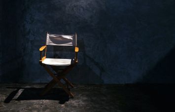 A single wood director's chair in a spotlight.