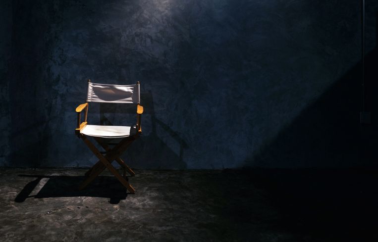 A single wood director's chair in a spotlight.